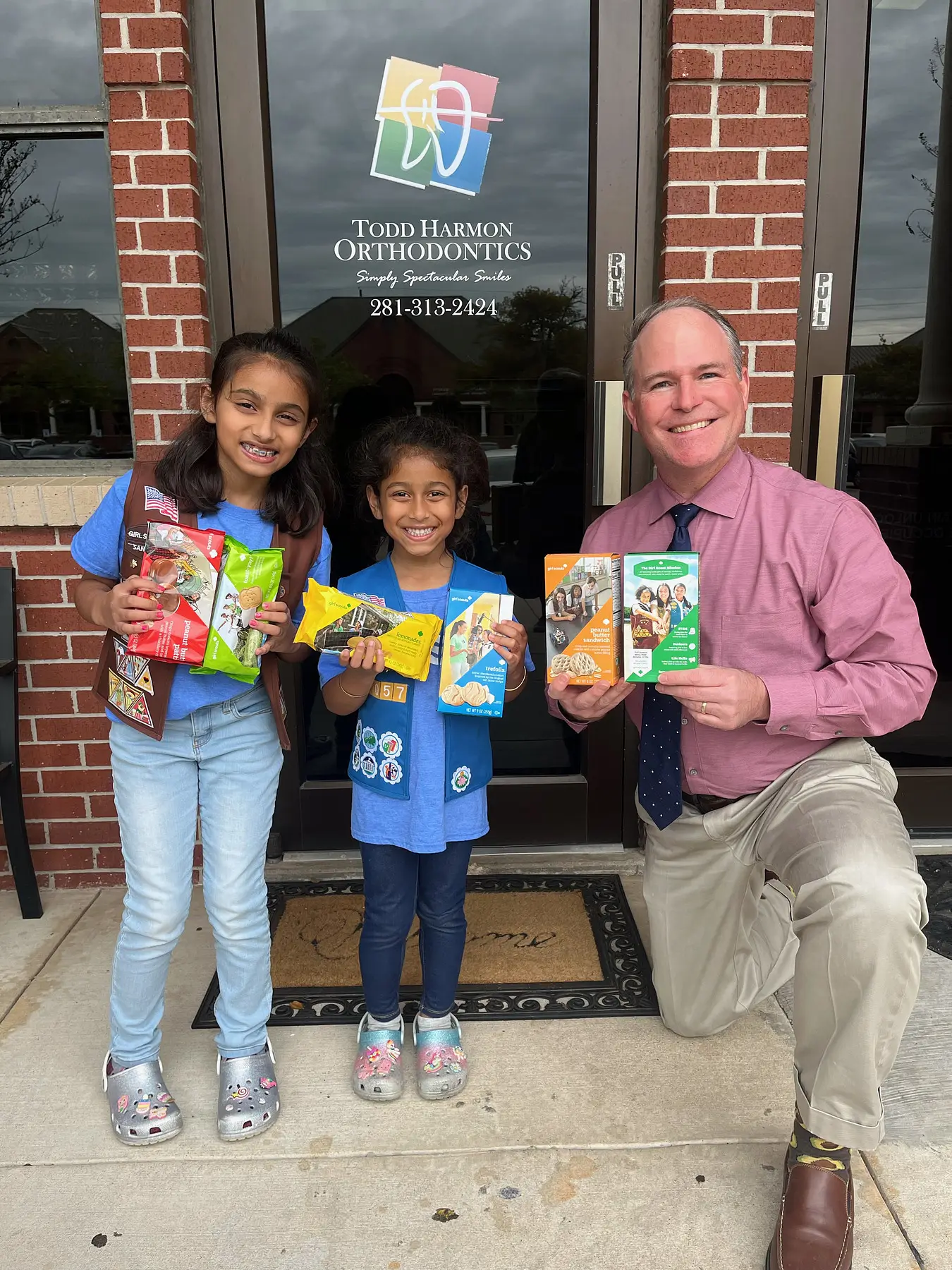 Dr. Harmon pictured with 2 girl scouts and a selection of girl scout cookies